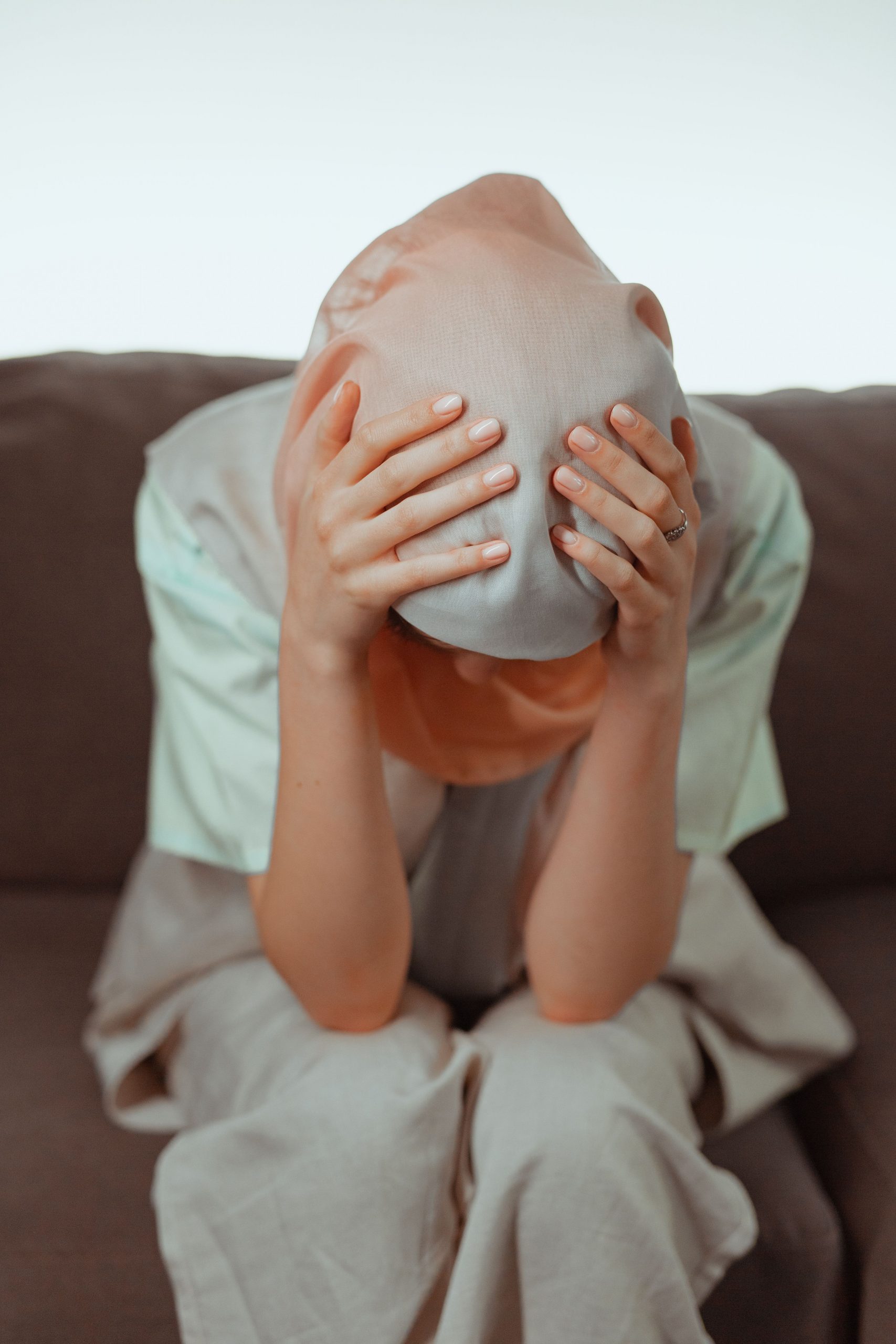 A woman sits on a couch with her head in her hands, expressing stress.